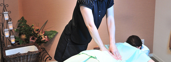  セラピストがうつ伏せになったお客様の背中をもみほぐしている場面です。