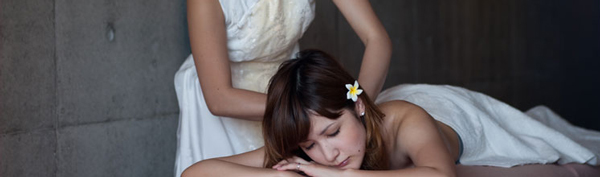 白っぽいノースリーブの衣装を着て背中や肩を施術しているセラピストの女性。